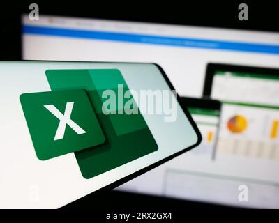 Smartphone con logo dell'editor di fogli di calcolo Microsoft Excel sullo schermo davanti al sito Web dell'azienda. Mettere a fuoco sul lato sinistro del display del telefono. Foto Stock