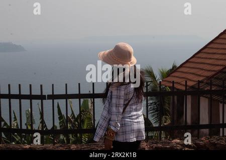 Vista posteriore di una donna elegante che ammira il paesaggio marino dalla terrazza recintata. Viaggiatore femminile in estate che guarda il bellissimo mare durante le vacanze Foto Stock