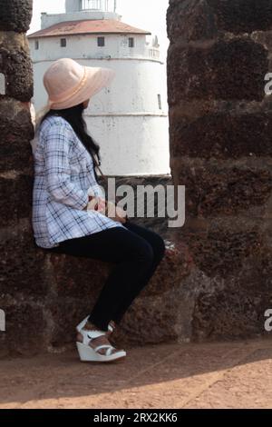 Donna turistica in cappello da sole che ammira il faro storico dal punto di osservazione. Viaggiatore femminile che si rilassa all'aperto durante le vacanze estive Foto Stock