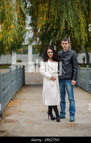 Un uomo abbraccia sua moglie incinta. Un uomo con una giacca nera abbraccia una donna con un cappotto bianco Foto Stock