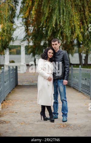 Un uomo abbraccia sua moglie incinta. Un uomo con una giacca nera abbraccia una donna con un cappotto bianco Foto Stock