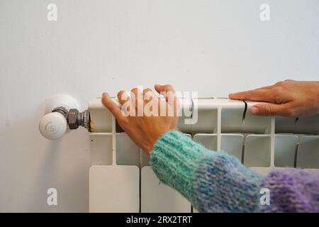 Donna che riscalda le mani sul radiatore di riscaldamento. Crisi energetica in Europa Foto Stock