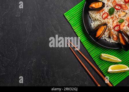 Riso fritto con frutti di mare cozze, gamberi e basilico in una piastra nera con bacchette in bambù verde mat e tavolo di pietra. Vista dall'alto. Foto Stock