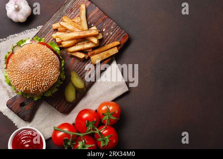 Hamburger fatti in casa con ingredienti di manzo, pomodori, lattuga, formaggio, cipolla, i cetrioli e le patatine fritte sul tagliere e rusty sfondo. Vista superiore Foto Stock