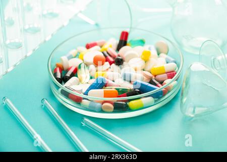 Piatto Petri con un mazzo di pillole e pinzette insieme a una siringa su sfondo blu. Foto di alta qualità Foto Stock