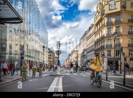 Persone in sella a biciclette elettriche noleggiate e a uno scooter elettrico vicino al grande magazzino Samaritaine in Rue de Rivoli, il negozio di marca alla moda Foto Stock