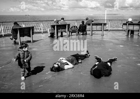 Un bambino piccolo guarda due passeggeri che dormiscono a bordo Di Un traghetto DFDS Cross Channel al largo della costa del Sussex, Regno Unito. Foto Stock