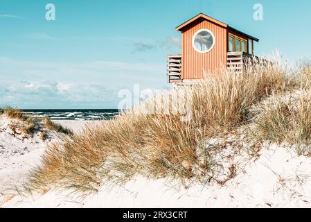 Torre di osservazione dei bagnini in legno rosso su palafitte presso il bar sulla spiaggia tra le dune di sabbia sulla spiaggia di Skanör med Falsterbo al sole del mattino, Skåne, Svezia Foto Stock