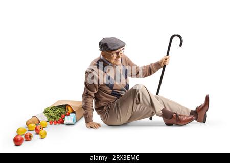 Uomo anziano con un bastone che cade sul pavimento con una borsa della spesa isolata su sfondo bianco Foto Stock