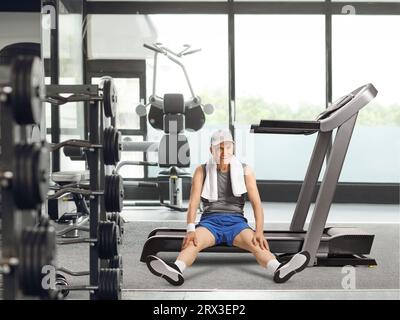 Un anziano anziano stanco seduto su un tapis roulant in palestra e sorridente Foto Stock