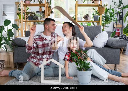 La famiglia tradizionale con bambino si sta godendo una nuova casa, seduto sul divano e tenendo il tetto. Mutuo, assicurazione e protezione, comprarmi e traslocare io Foto Stock