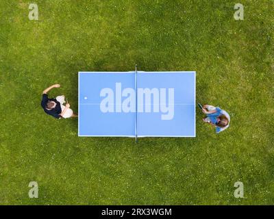 Vista aerea persone che giocano a ping pong all'aperto. Vista dall'alto due ragazzi che giocano a ping pong su un prato verde. Sport all'aperto con vista aerea Foto Stock