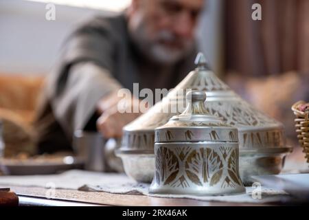 Latta araba ornata su un tavolo del soggiorno con un vecchio arabo sullo sfondo Foto Stock