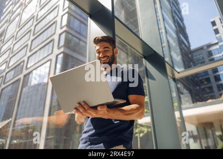 Uomo d'affari elegante che lavora su un computer portatile mentre si trova in ufficio vicino a uno sfondo di finestre Foto Stock
