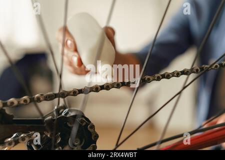 Primo piano di un bell'uomo in abbigliamento casual lubrificare la catena della bicicletta con olio a casa Foto Stock