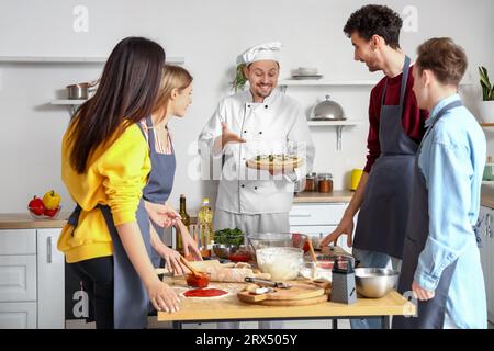 Italian chef with prepared pizza and group of young people after cooking class in kitchen Stock Photo