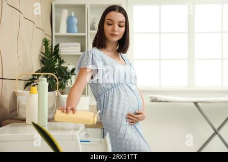 Giovane donna incinta che fa il bucato a casa Foto Stock