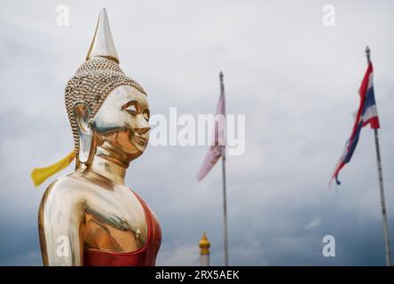 Statua di Buddha di colore dorato con bandiere e suggestivo paesaggio nuvoloso in cima al Tempel della Grotta della Tigre, Wat Tham sua, a Krabi, Thailandia Foto Stock