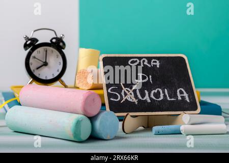 Gessetti di varie dimensioni e colori con una lavagna accanto con tempo scolastico scritto in italiano Foto Stock