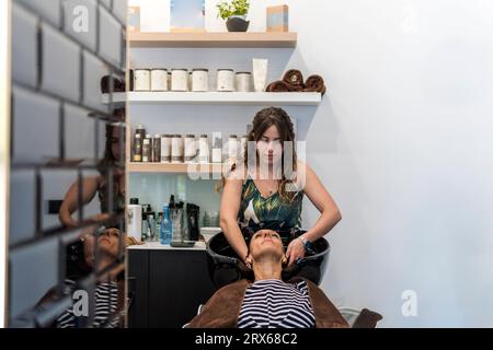 Giovane parrucchiere che lava i capelli di una donna al salone Foto Stock