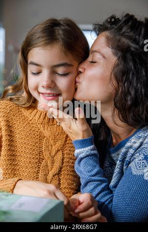 Madre che bacia figlia sorridente a casa Foto Stock