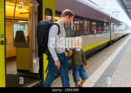 Figlio e padre felici che camminano sul binario di fronte al treno Foto Stock