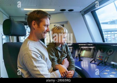 Un uomo con un aspetto europeo di 40 anni e suo figlio biondo di 5 anni siedono nella cabina del conducente del treno Foto Stock