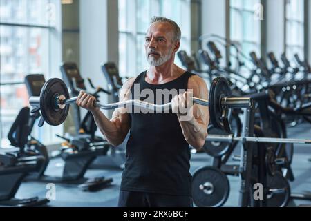 Uomo maturo barbuto che si esercita con il campanello nel centro benessere Foto Stock