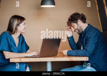 Donna d'affari sorridente che usa un computer portatile e parla con un uomo d'affari nell'ufficio Foto Stock