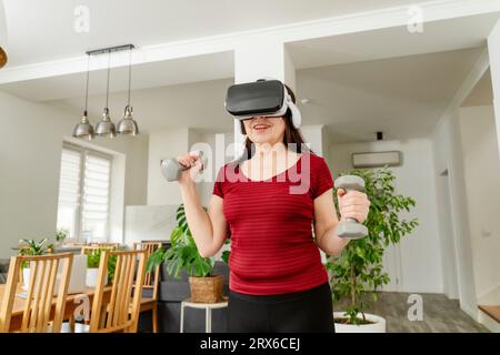 Donna che usa galsse VR e che si allena con i manubri a casa Foto Stock