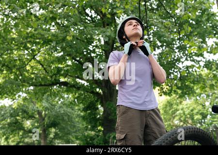 Donna che fissa il casco sotto l'albero nella foresta Foto Stock
