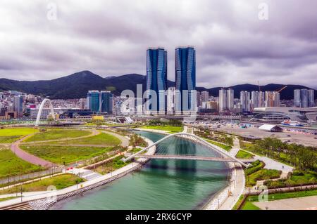 Corea del Sud, Busan, cielo nuvoloso sul ponte sul fiume che scorre attraverso il parco cittadino Foto Stock