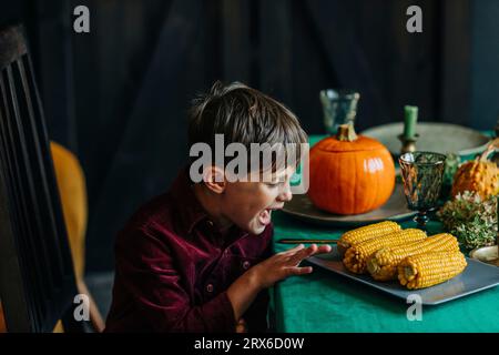 Happy boy che tocca il mais dolce al tavolo da pranzo Foto Stock