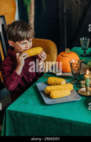 Un ragazzo premuroso che mangia mais dolce al tavolo da pranzo Foto Stock