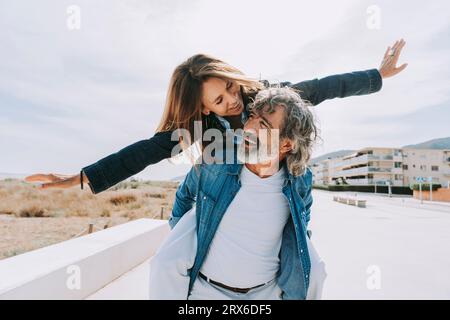 Donna anziana che si diverte a fare piggybacking su un uomo vicino alla spiaggia Foto Stock