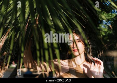 Giovane donna tra le foglie di palma nelle giornate di sole Foto Stock