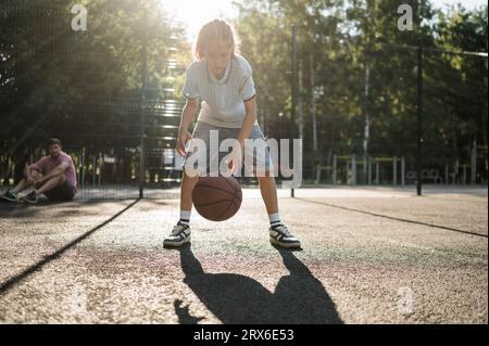 Ragazzo che dribbling basket con padre in sottofondo Foto Stock