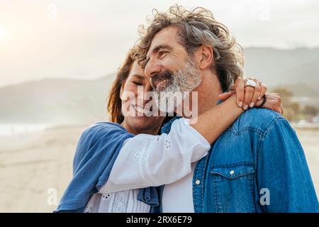 Donna sorridente che abbraccia l'uomo in spiaggia Foto Stock