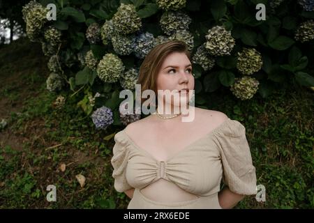 Donna contemplativa in piedi di fronte a piante di fiori di ortensia Foto Stock