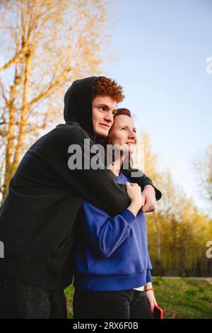 Ragazzo adolescente che abbraccia la madre nel parco Foto Stock