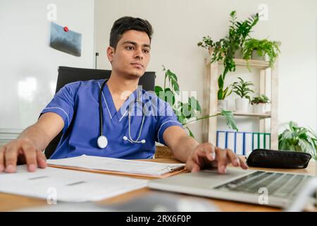 Giovane medico maschio che lavora sul computer portatile alla scrivania della clinica Foto Stock