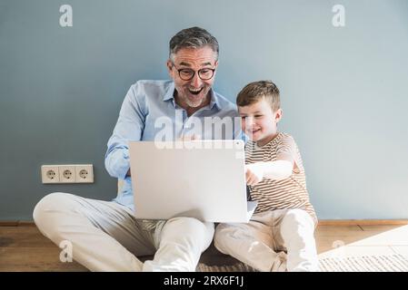 Nonno e nipote allegri che usano il portatile a casa Foto Stock