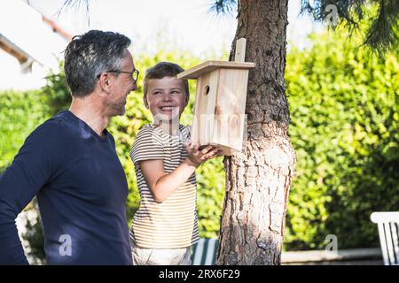 Felice ragazzo che fissa la casa degli uccelli sull'albero dal nonno nel cortile posteriore Foto Stock