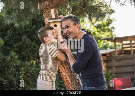 Felice nonno e nipote che riparano la casa degli uccelli sull'albero Foto Stock