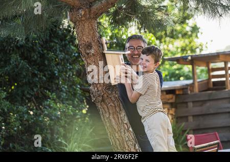 Ragazzo sorridente appeso a casa degli uccelli sull'albero con il nonno Foto Stock