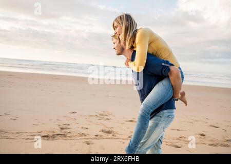 Un uomo sorridente che fa un giro in barca a una donna in spiaggia Foto Stock