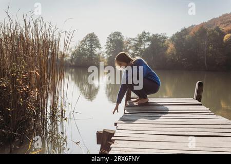 Donna che si avvicina all'acqua al molo nelle giornate di sole Foto Stock