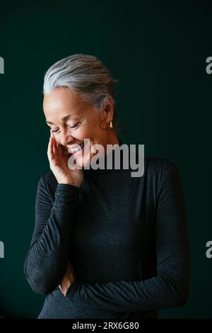 Donna matura felice che tocca il volto davanti al muro Foto Stock