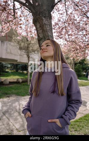 Donna premurosa con le mani nelle tasche appoggiate al tronco di ciliegio Foto Stock