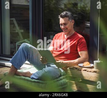 Uomo che si rilassa sul balcone con un tablet digitale nelle mani Foto Stock